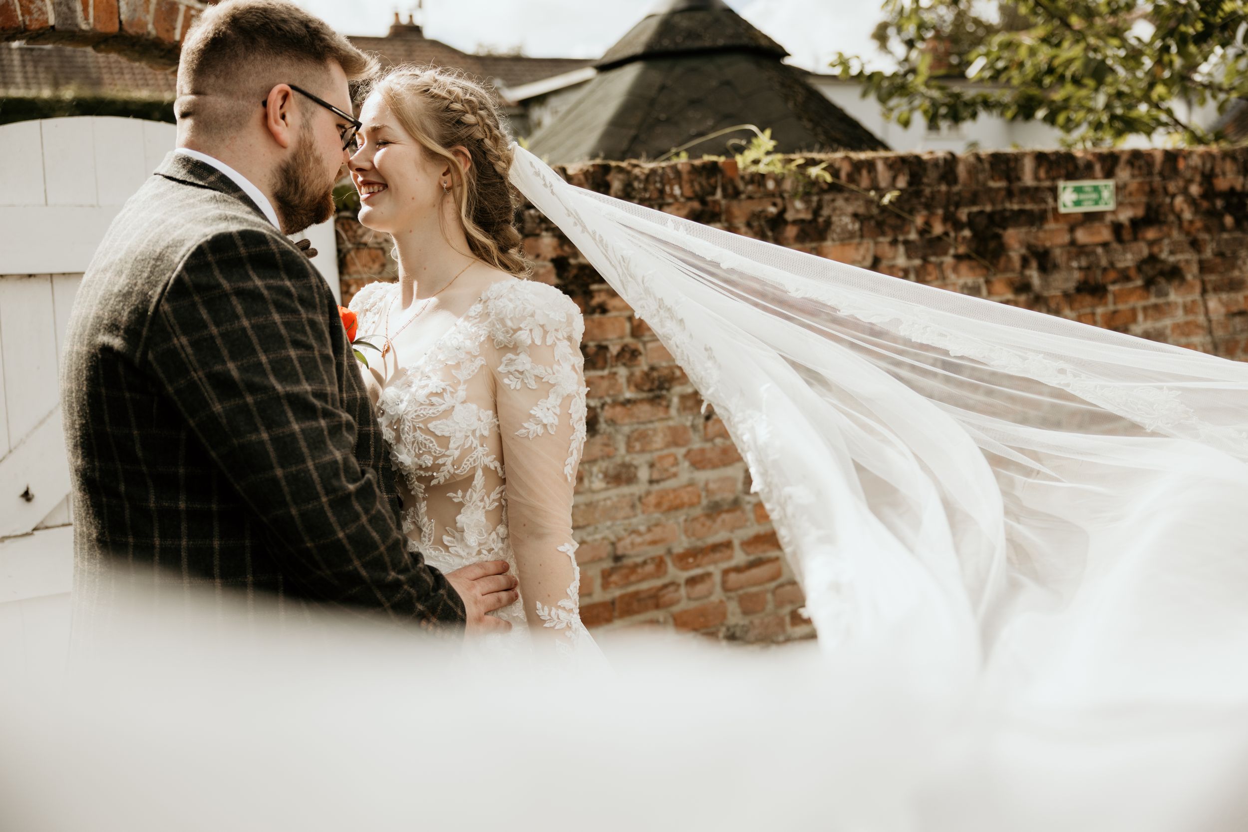 A couple shares an intimate moment as the bride's veil flows dramatically in the wind.