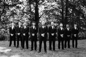 Groomsmen in matching black suits and bowties lined up outdoors.