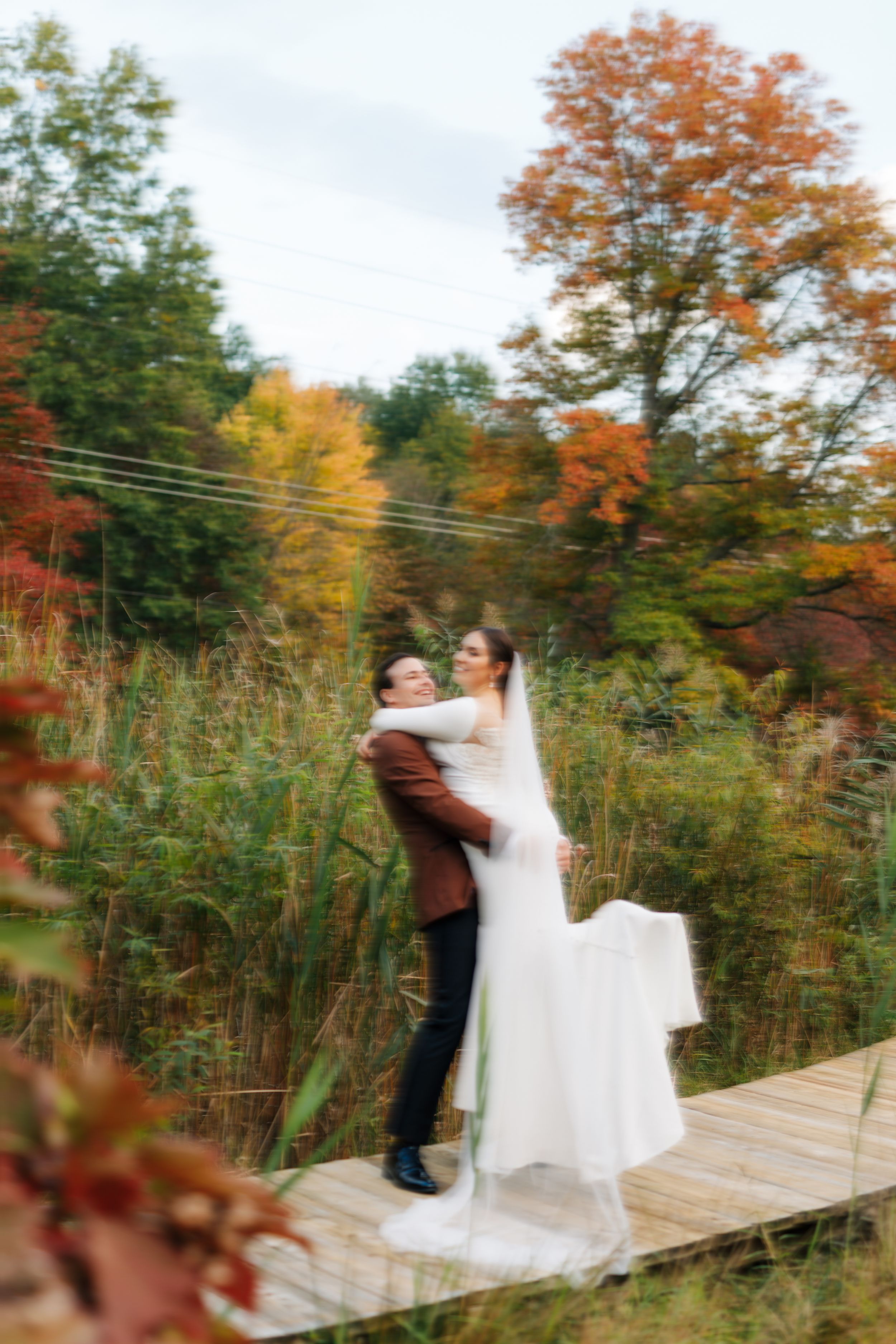 A blurred romantic moment captured on a wooden bridge with autumn foliage in the background.
