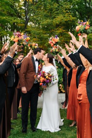 Wedding guests raise their hands in celebration as the couple shares a moment surrounded by colorful fall bouquets.