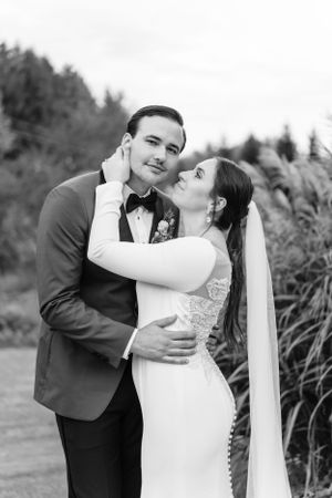 A tender black and white portrait of a couple in wedding attire embracing outdoors.