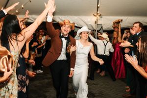 Wedding guests dance and celebrate with raised hands under a reception tent.