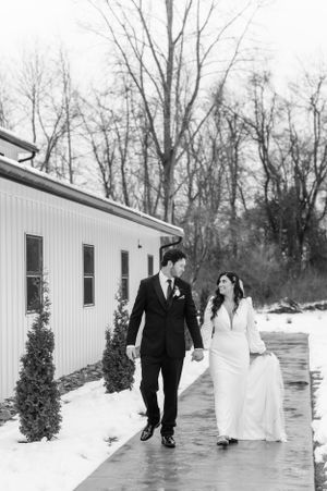 A black and white photo of a couple walking together along a modern building in winter.