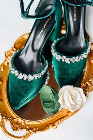 Elegant emerald velvet heels with crystal embellishments displayed on a gold ornate tray.