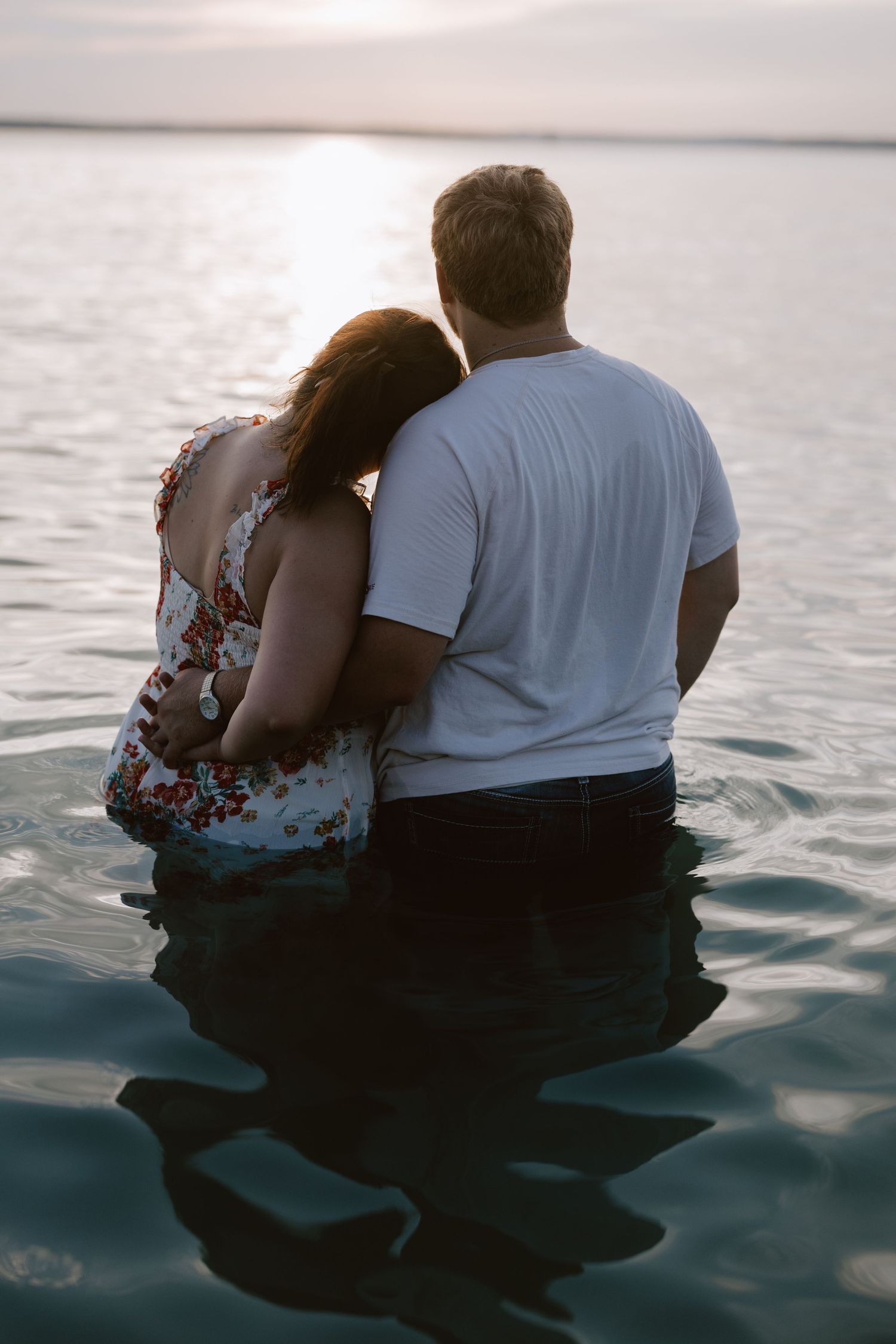 Couple sitting in water watching sunset together at beach.