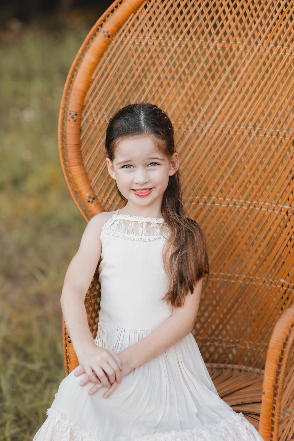 A white wicker peacock chair features a lovely white dress against a natural outdoor setting.