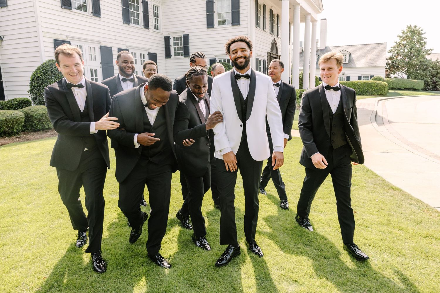 Group of men in matching cream suits posing together on a wooden deck outdoors.