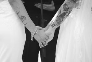 Black and white photo of tattooed hands holding during a wedding ceremony.