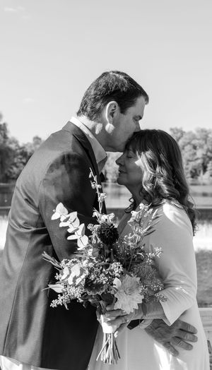 A romantic black and white wedding photo of a couple sharing an intimate moment with a beautiful floral bouquet.