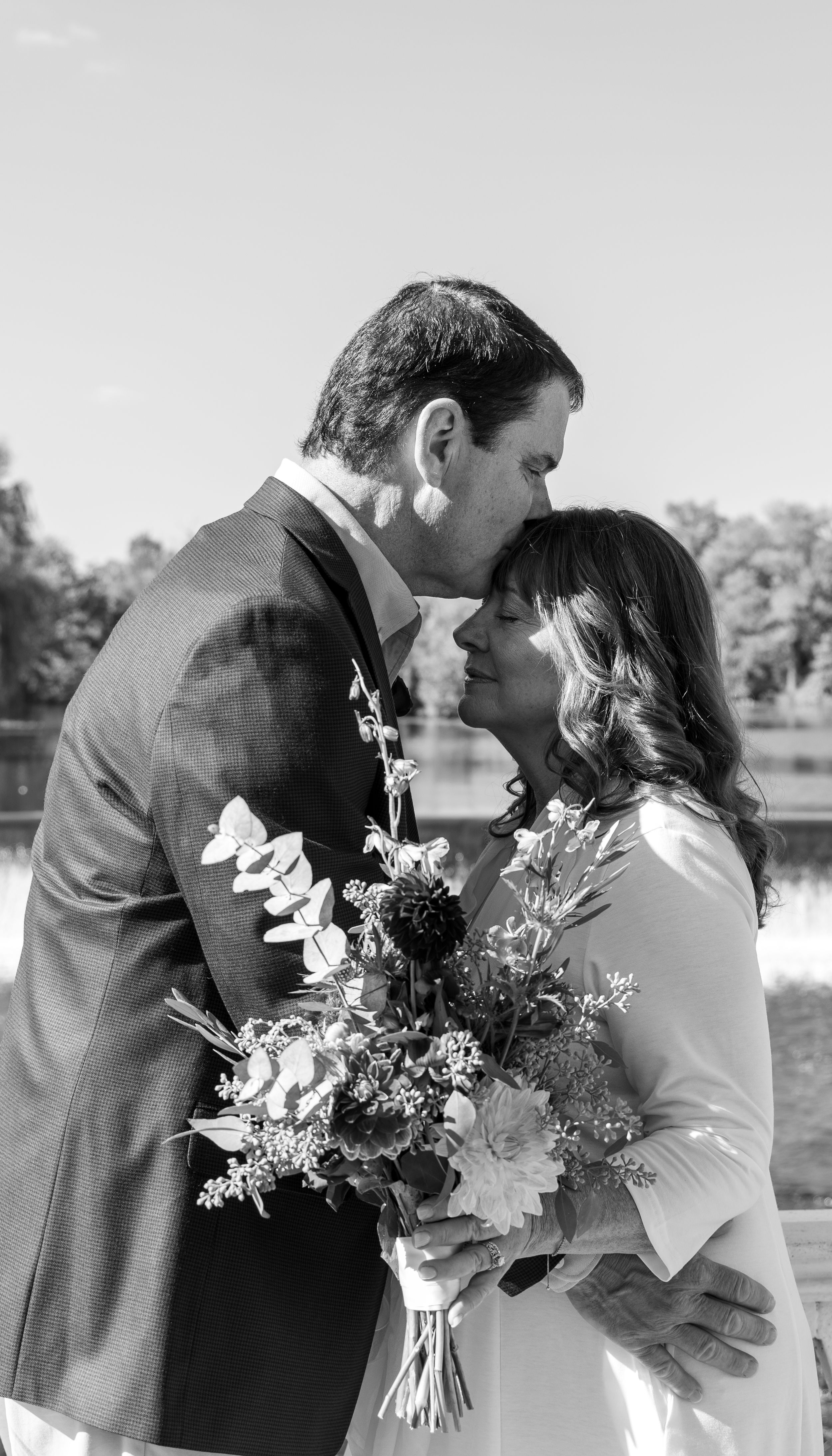 A romantic black and white wedding photo of a couple sharing an intimate moment with a beautiful floral bouquet.