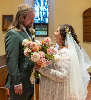 A couple shares a joyful moment during their wedding ceremony in a church with pink floral bouquet.