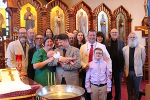 Group gathered for a baptism ceremony in front of decorative church iconostasis.