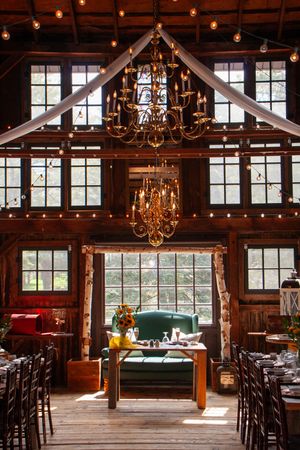 Rustic barn venue with elegant chandeliers and wooden beams set up for a wedding ceremony.