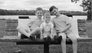 Three siblings share a moment together on a park bench in black and white photography.