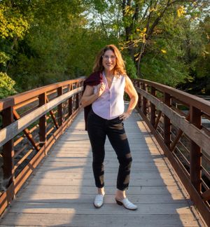 Full body portrait of woman on wooden bridge with autumn trees in background.