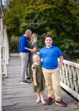 Outdoor family portrait on a wooden bridge near a historic red building.