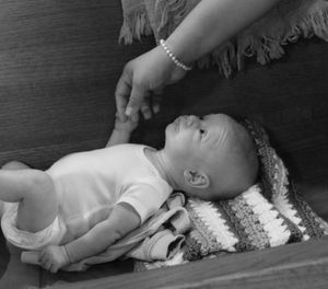 A vintage black and white photograph showing a baby lying on a decorative pillow.
