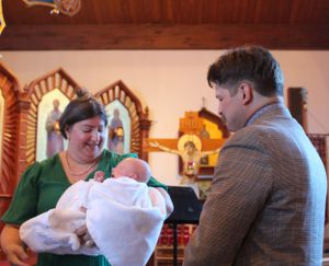 A baptism ceremony taking place inside a church with ornate religious icons in the background.