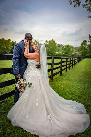 Elegant wedding dress with flowing train photographed against black fence and green countryside.