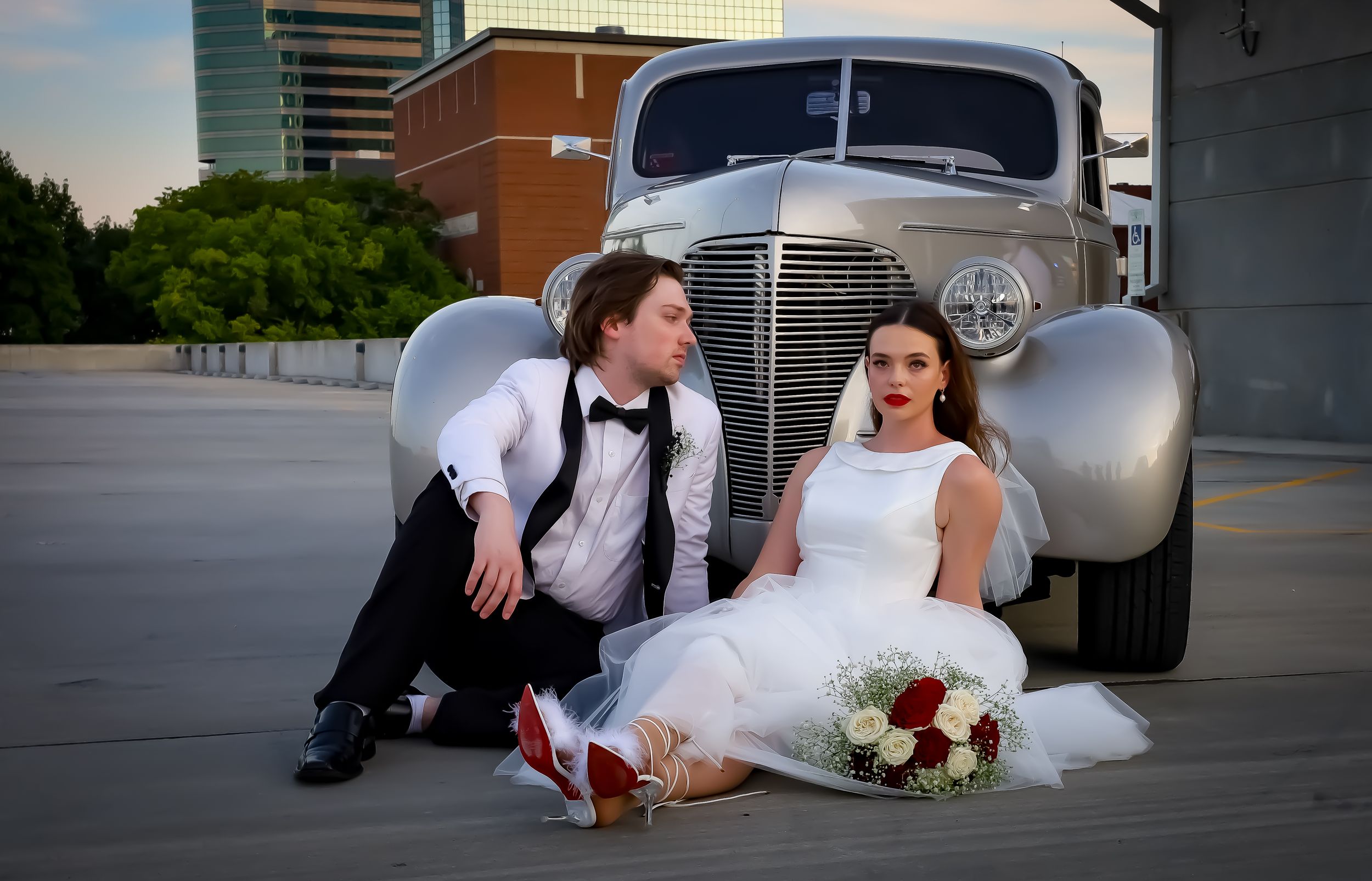 Playful wedding couple poses with vintage car during sunset photoshoot.