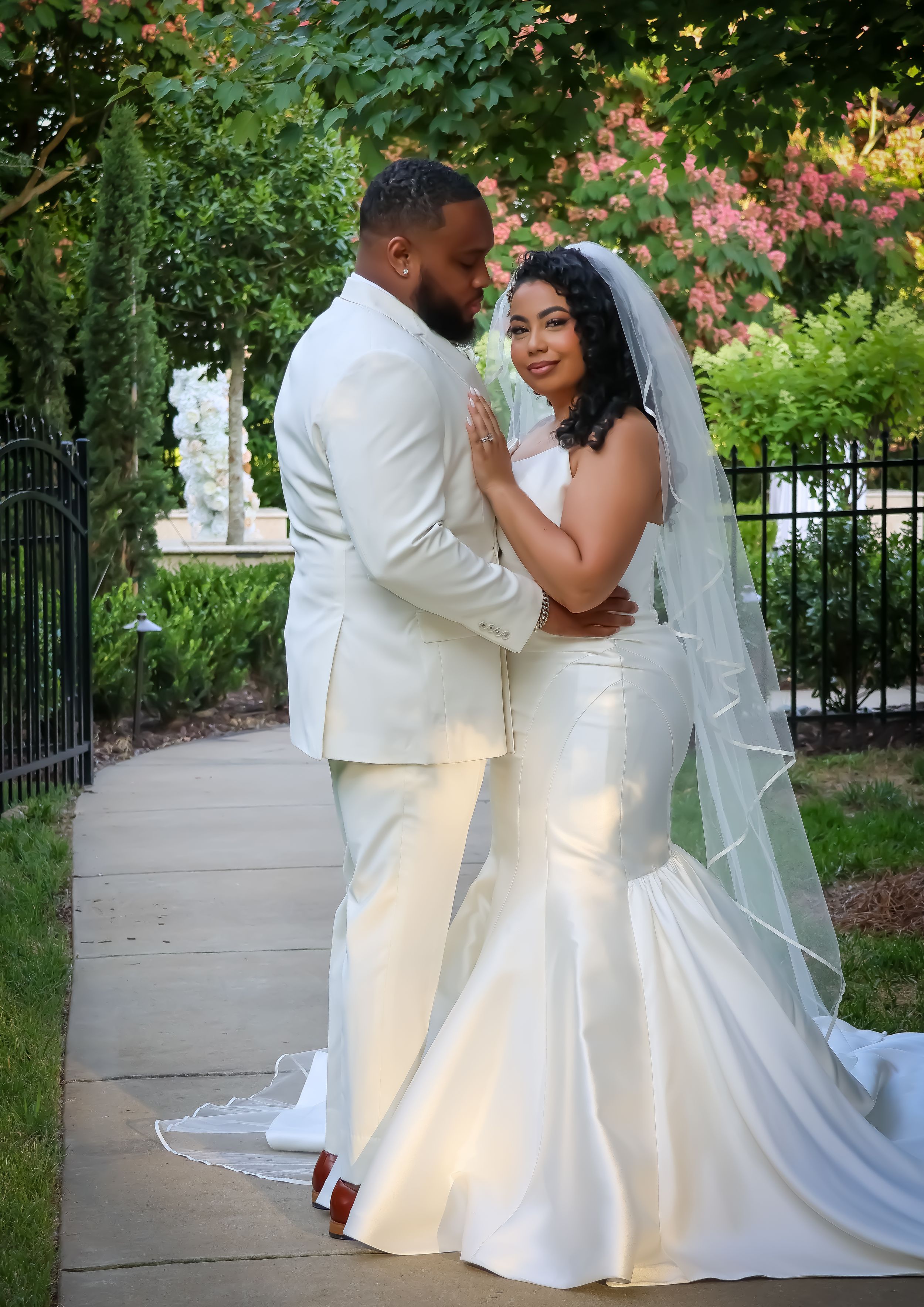Newlyweds in white attire share intimate moments in a garden setting.