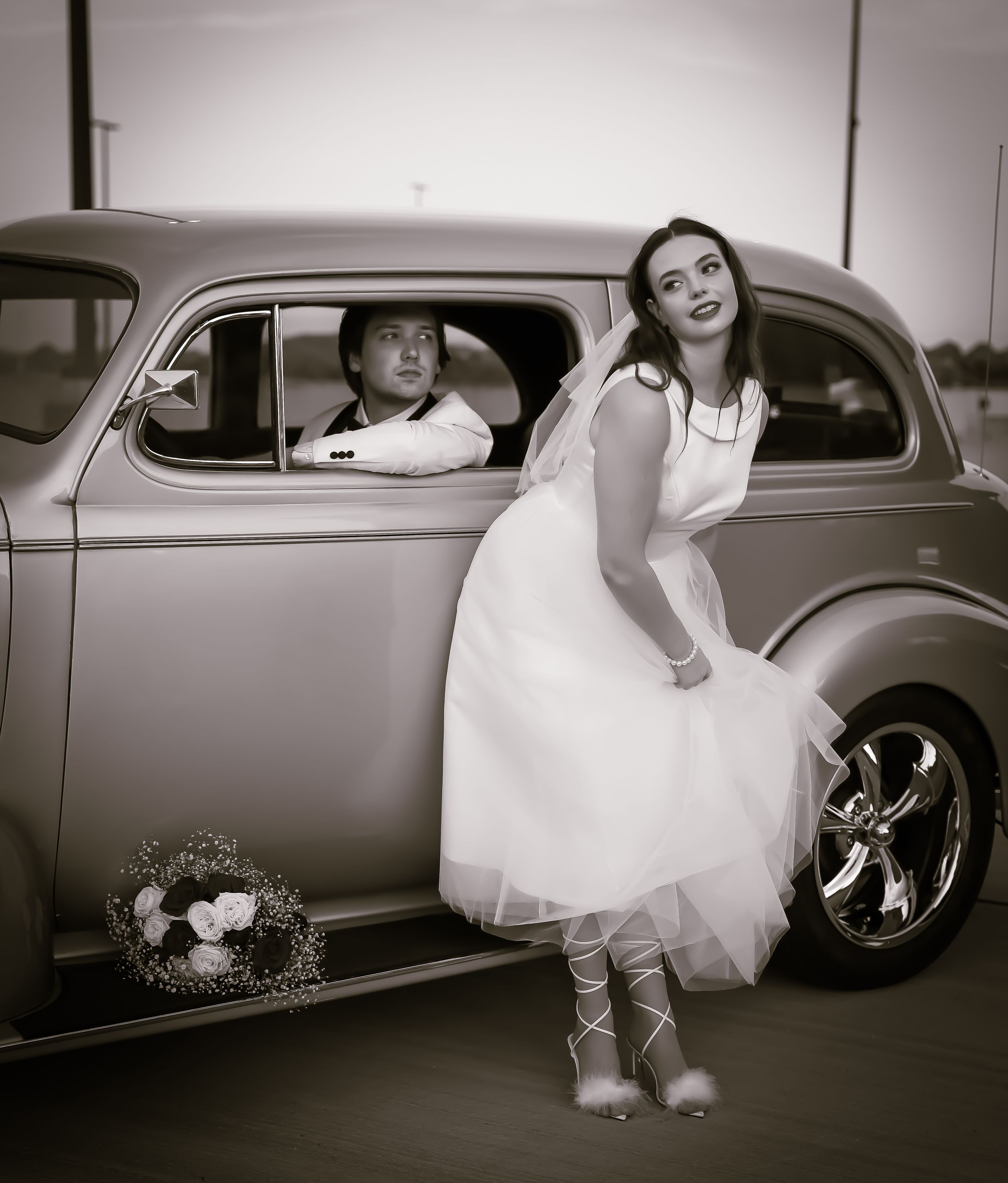 Black and white wedding photos with classic car showing playful bride and groom moments.