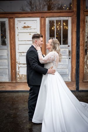 Couple dancing in vintage-style venue with weathered white doors and string lights.