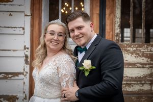 Wedding portraits against rustic wooden backdrop with vintage white doors and warm lighting.