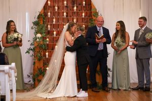 Wedding ceremony venue decorated with brick wall backdrop and floral arrangements.