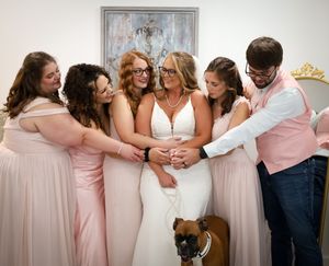 Bridesmaids in pink dresses pose together against a white wall with artwork.