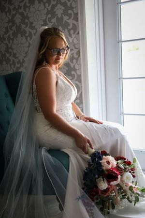 Wedding dress details captured in a window-lit room with floral bouquet.