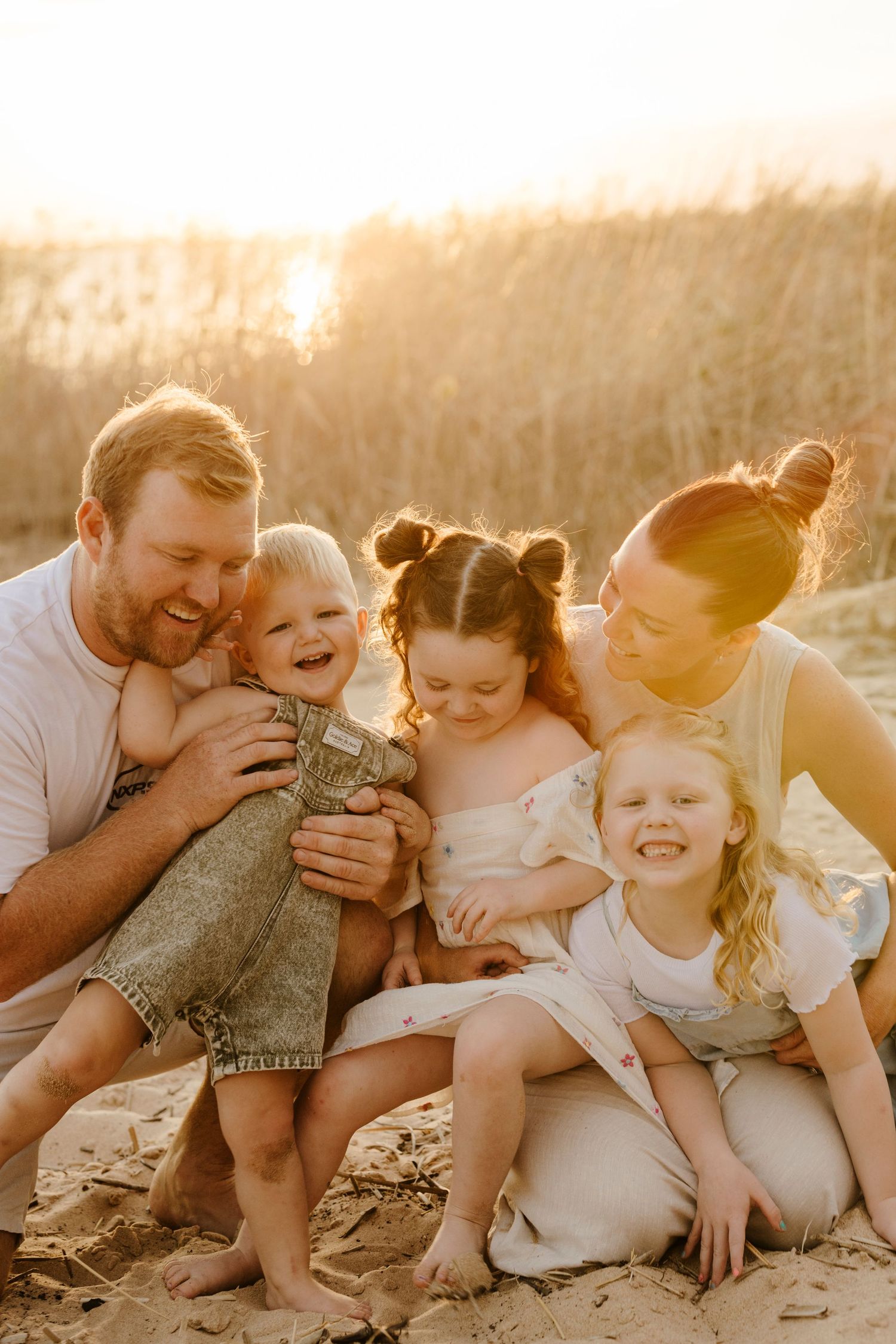 A joyful family of five shares a warm embrace on a sandy beach during a golden sunset.