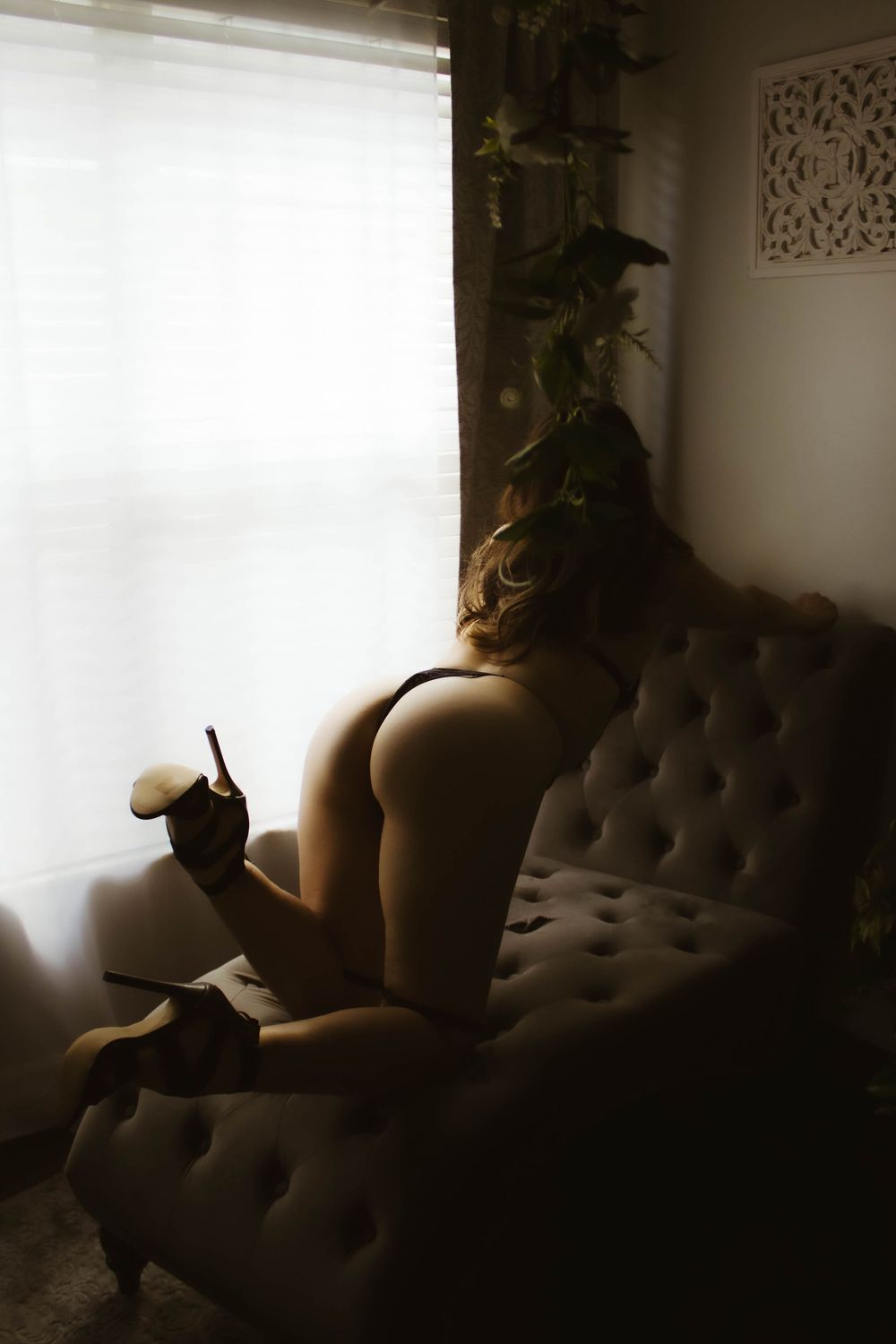 Artistic silhouette of a figure reclining on tufted furniture in moody lighting with dramatic shadows.