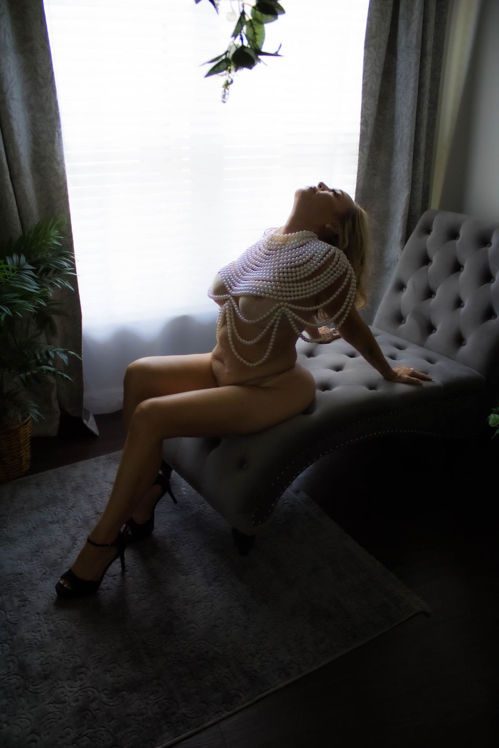 A person in a white dress reclines on a gray tufted sofa near a window with soft natural lighting.