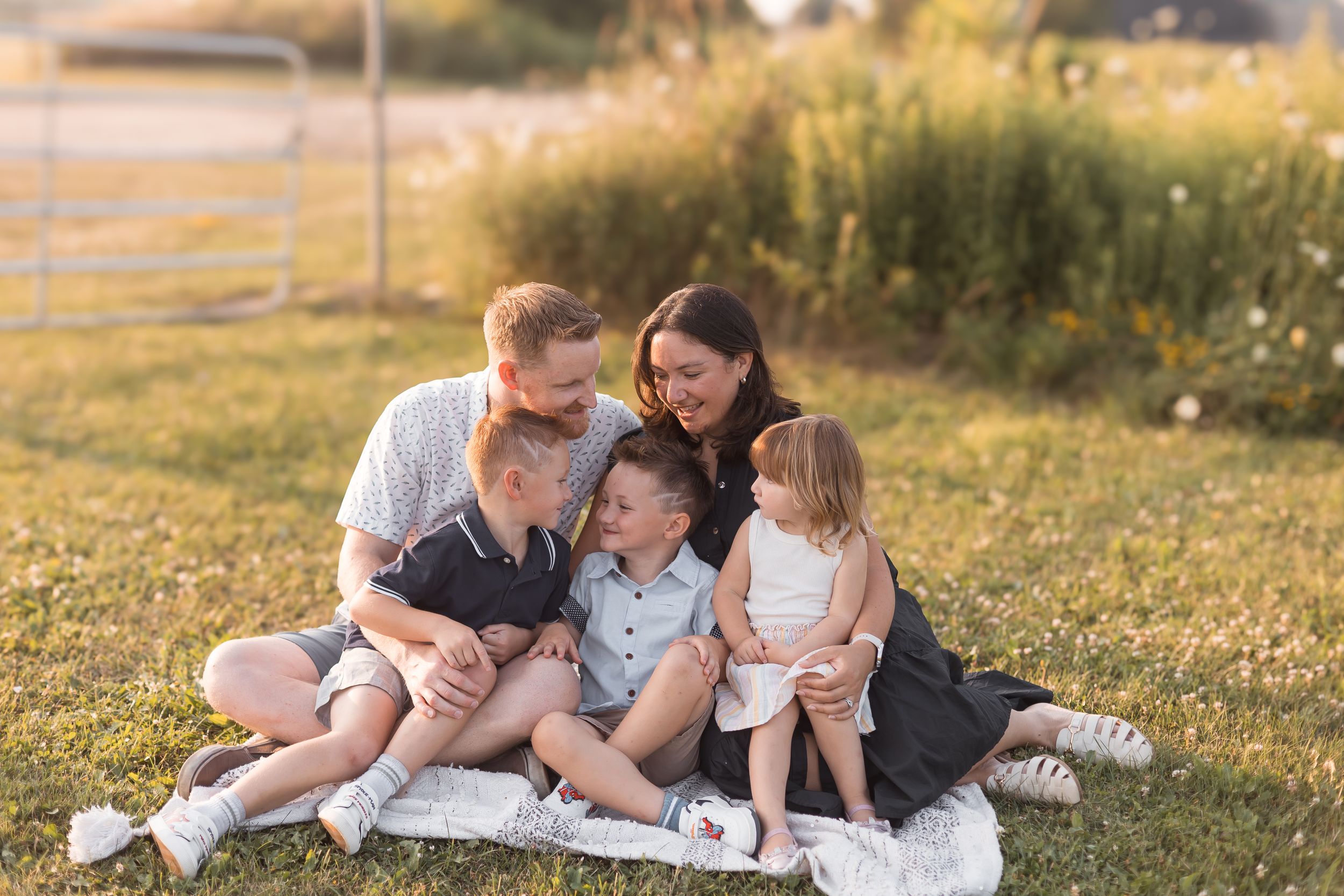 Family of five cuddling together on blanket in sunny outdoor field.