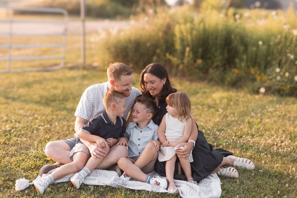 Family of five cuddling together on blanket in sunny outdoor field.