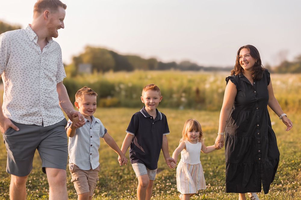 Joyful family of five holding hands walking through a sunny green meadow.