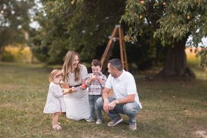Happy family of four sharing apples outdoors near a tree on a sunny day.
