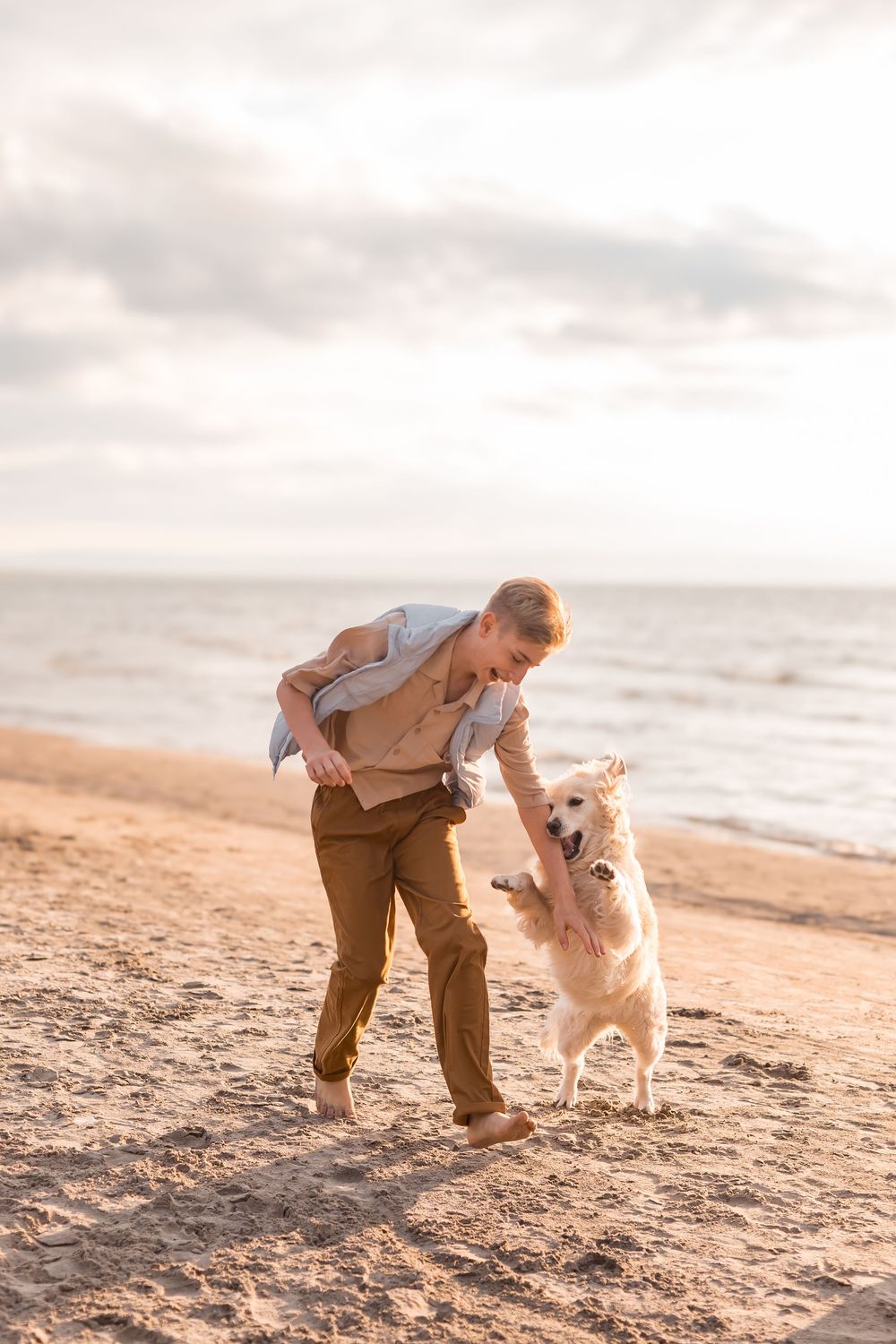 Man playing with golden retriever dog on sandy beach at sunset.