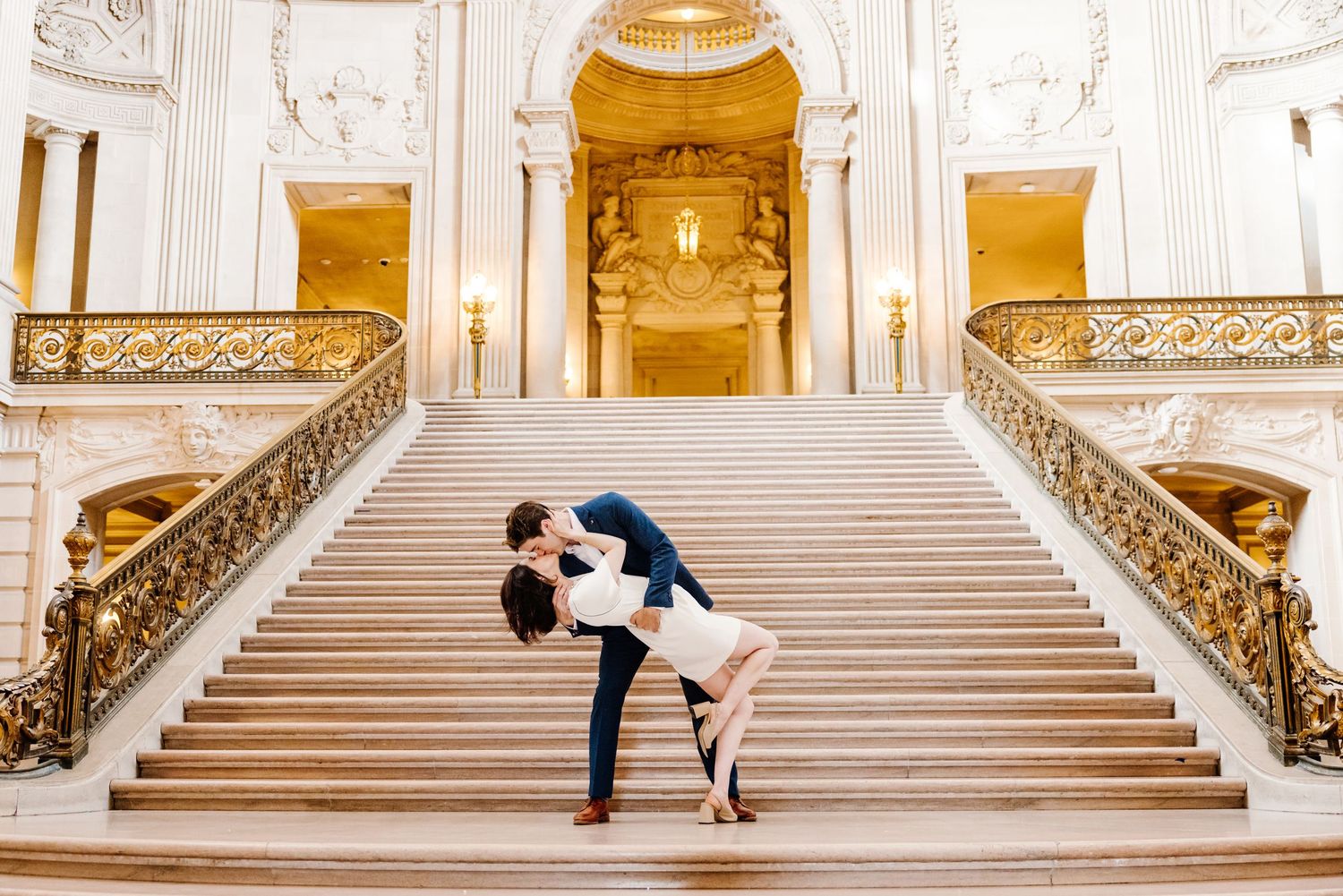 Happy newlyweds celebrate joyfully on an open field with a stately building in the background.