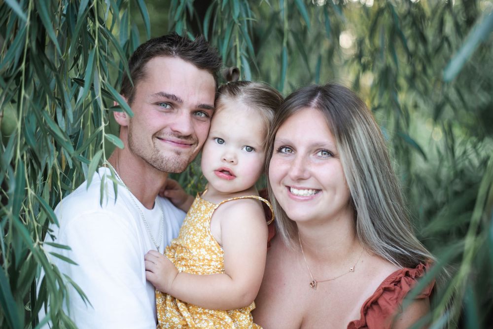 Family portrait among tall grass with warm sunset lighting in background.