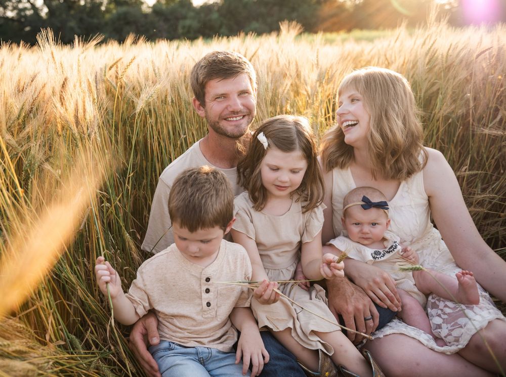 Family sitting together in golden wheat field during sunset.