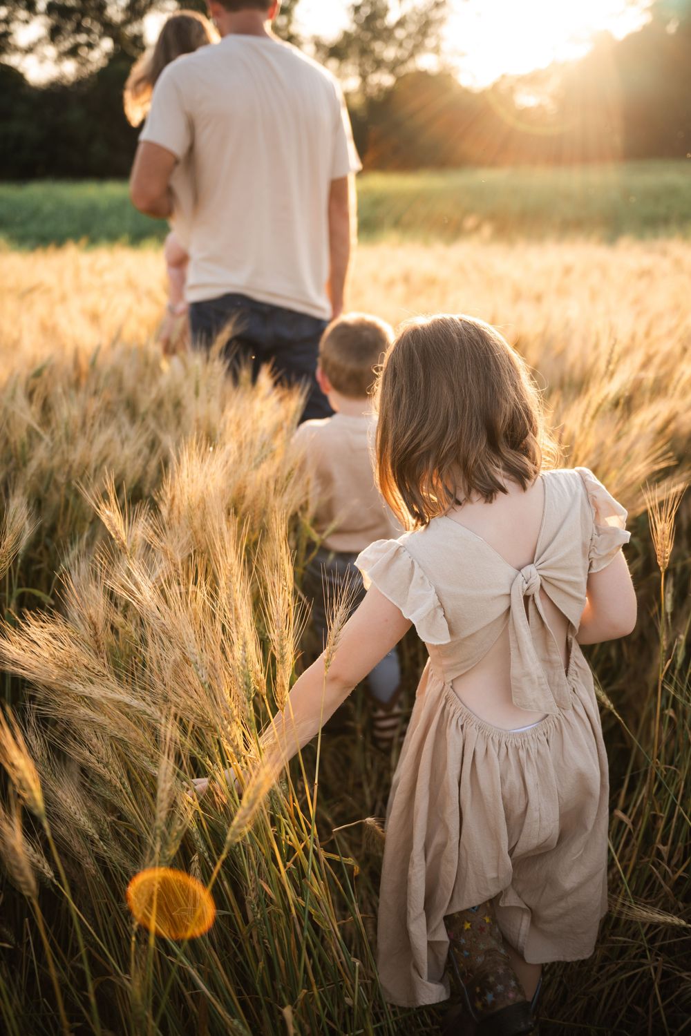 Children walking through tall wheat field at golden hour.