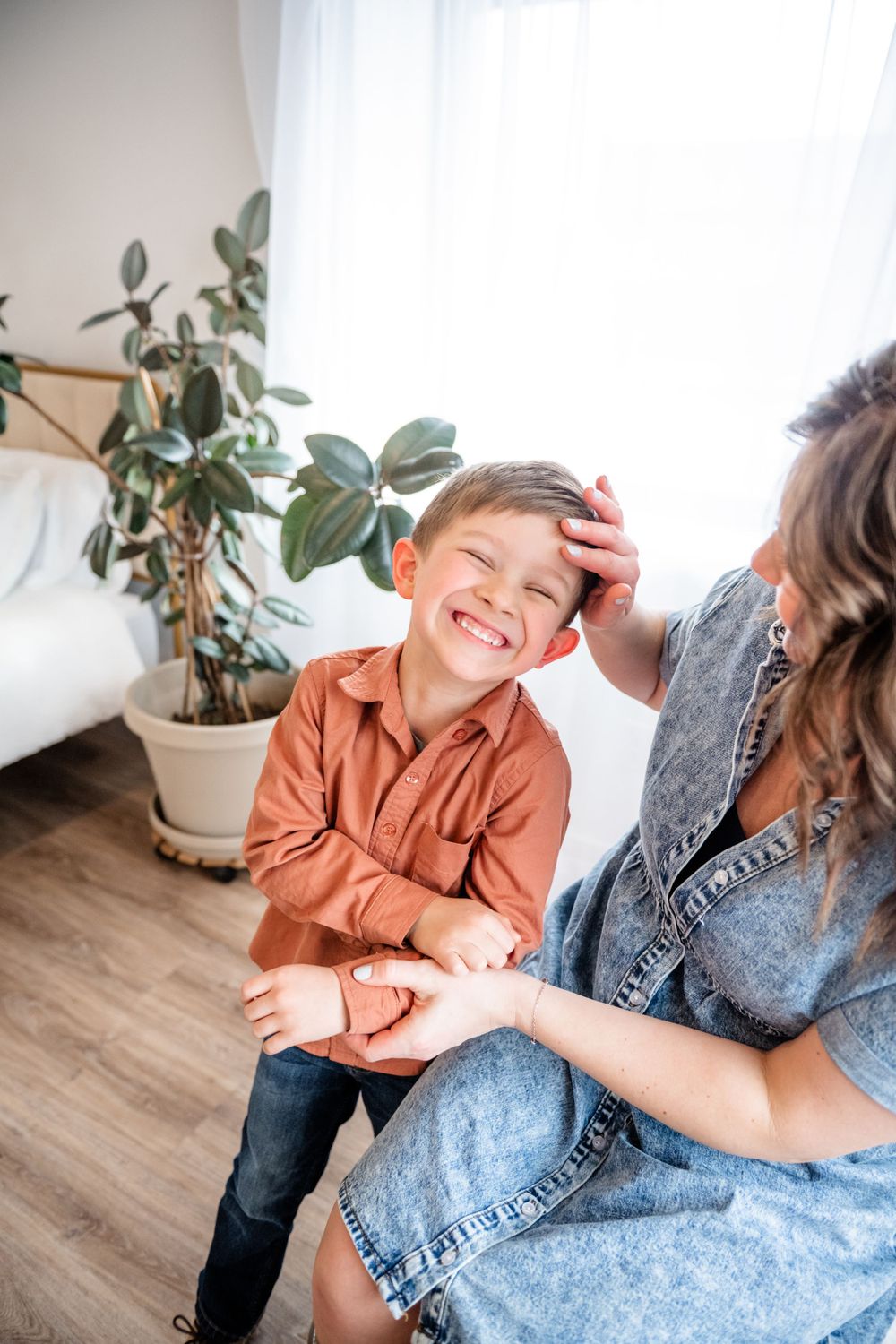 Candid moment between family members laughing together in bright indoor setting with plants.