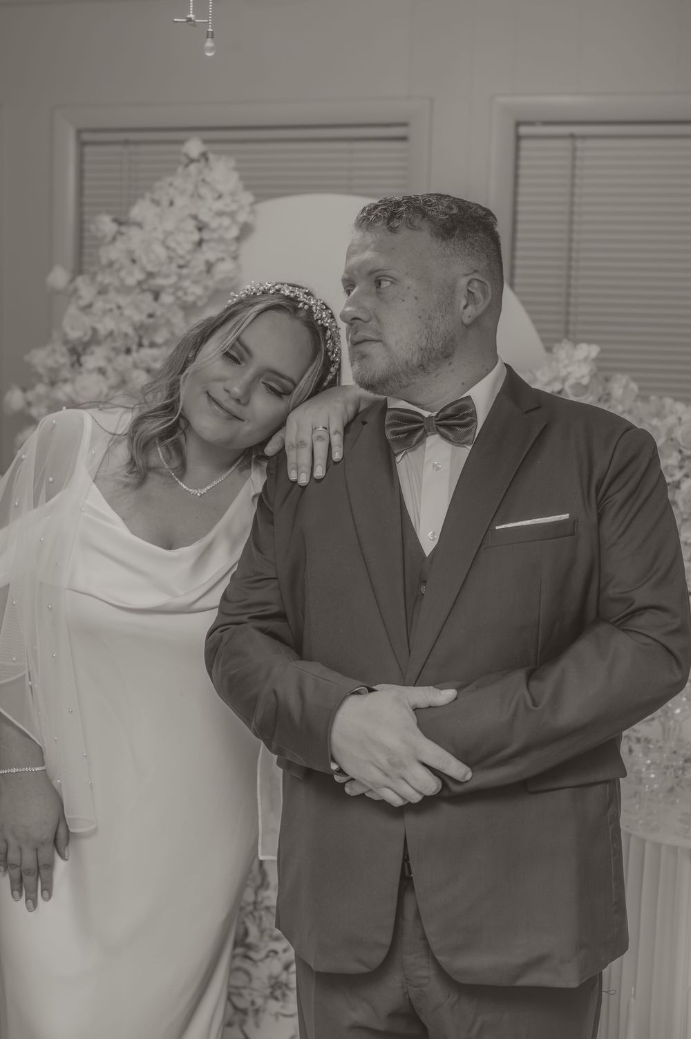 A romantic black and white wedding photo showing a bride in white dress and groom in tuxedo with bow tie.