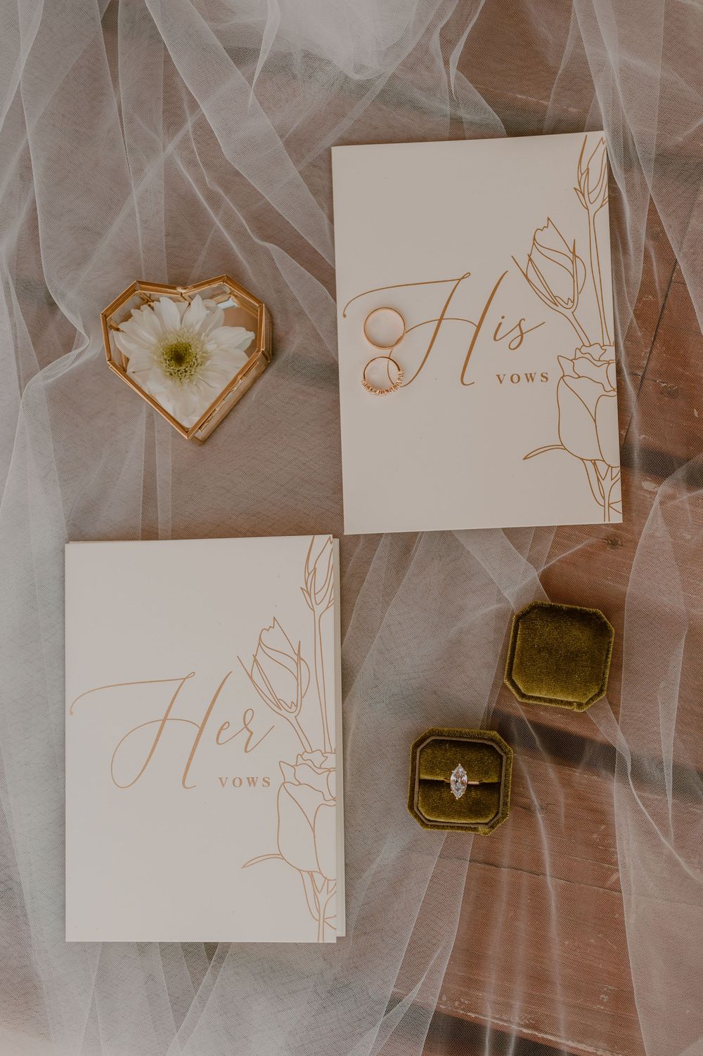 Wedding vow books labeled 'His' and 'Hers' with velvet ring boxes and heart-shaped decor on tulle fabric background.