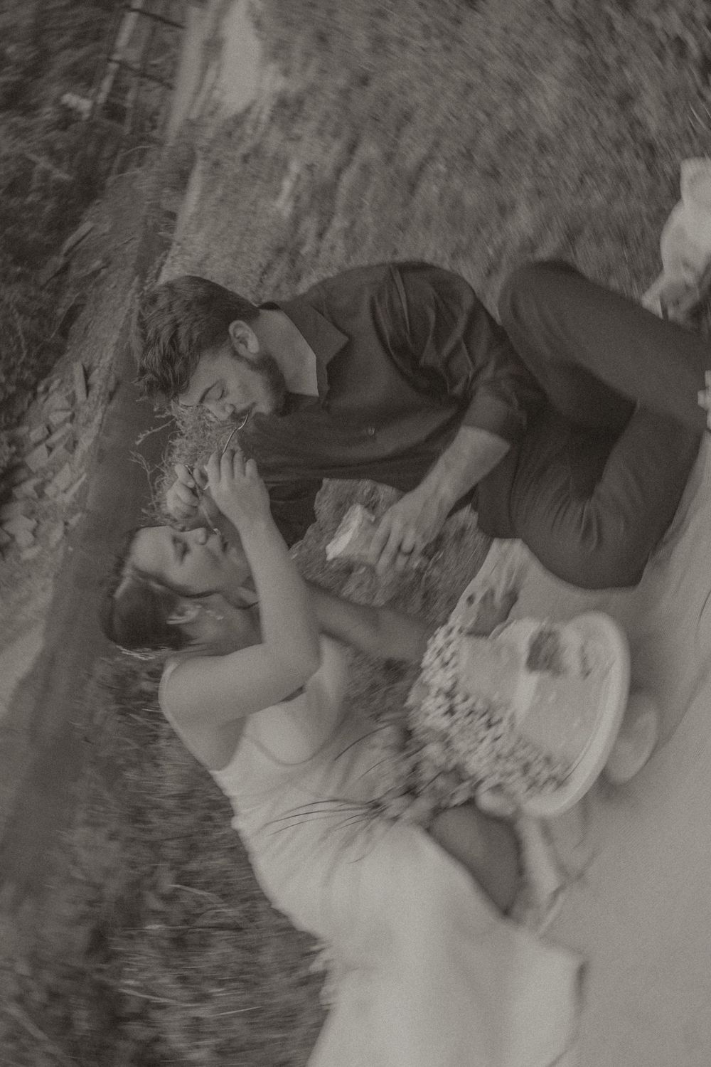 Black and white photo of a romantic couple sharing an intimate moment outdoors, lying together on the ground.