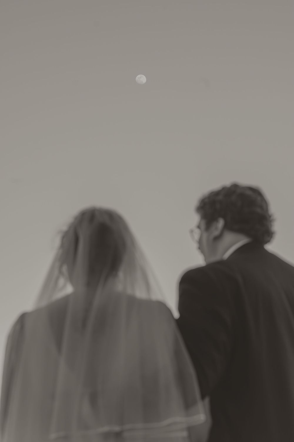Black and white photo of bride and groom viewing full moon in sky.