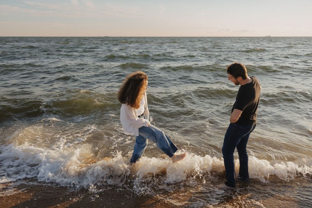 A couple frolicks and plays together in the waves at sunset along a beautiful ocean beach.