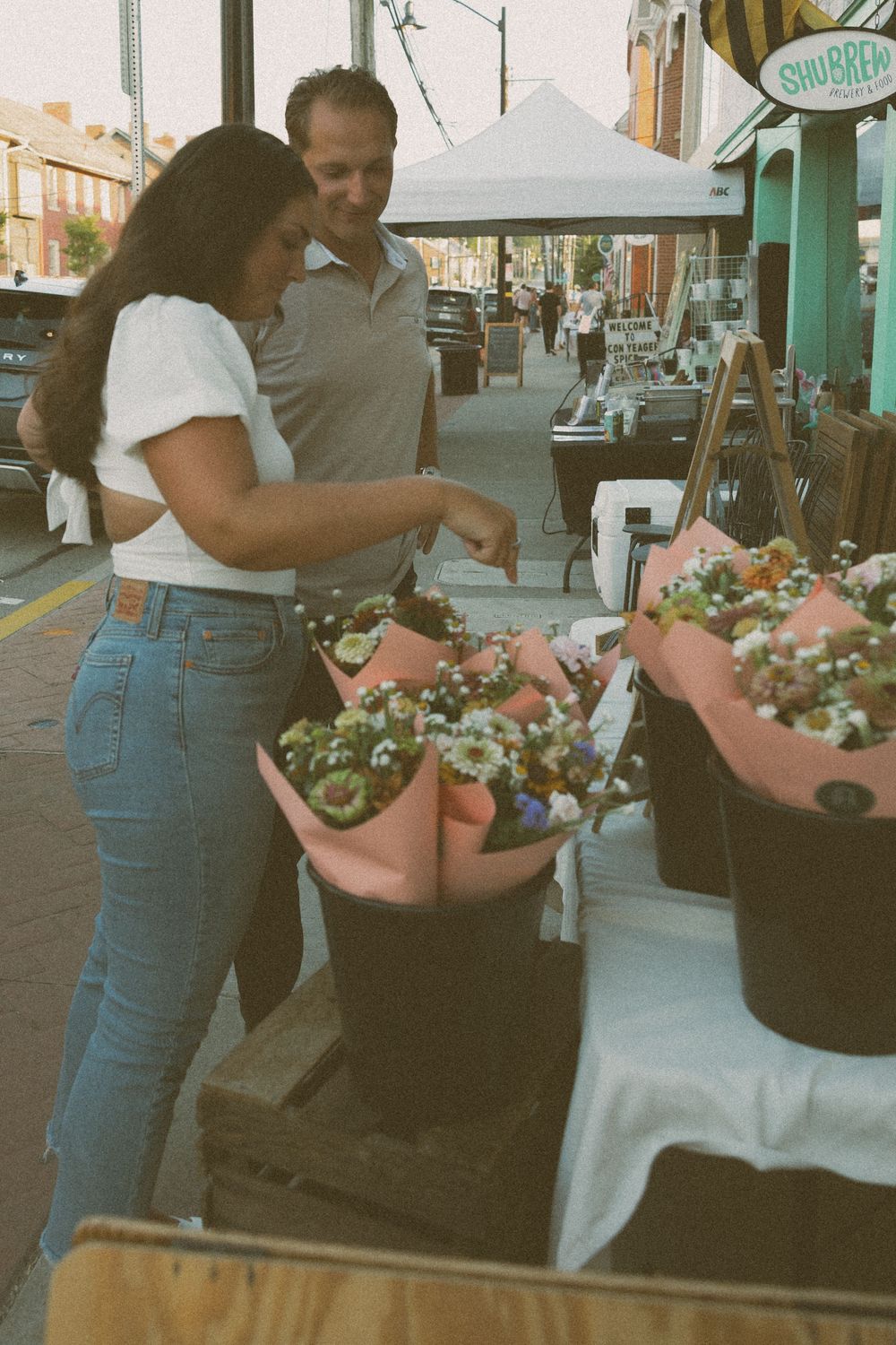 A shopper selects fresh colorful produce from a market stall on a city sidewalk.